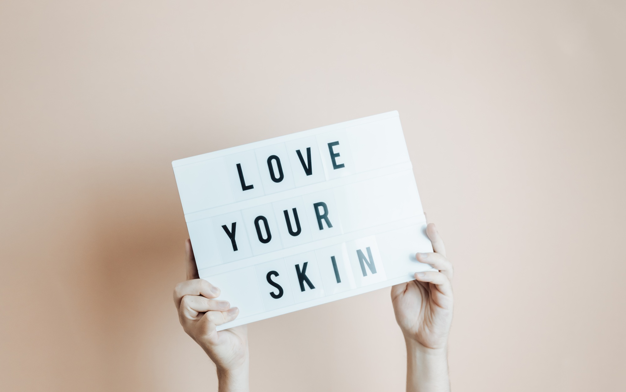 Hands holding a sing with love your skin written in it, minimal desaturated background